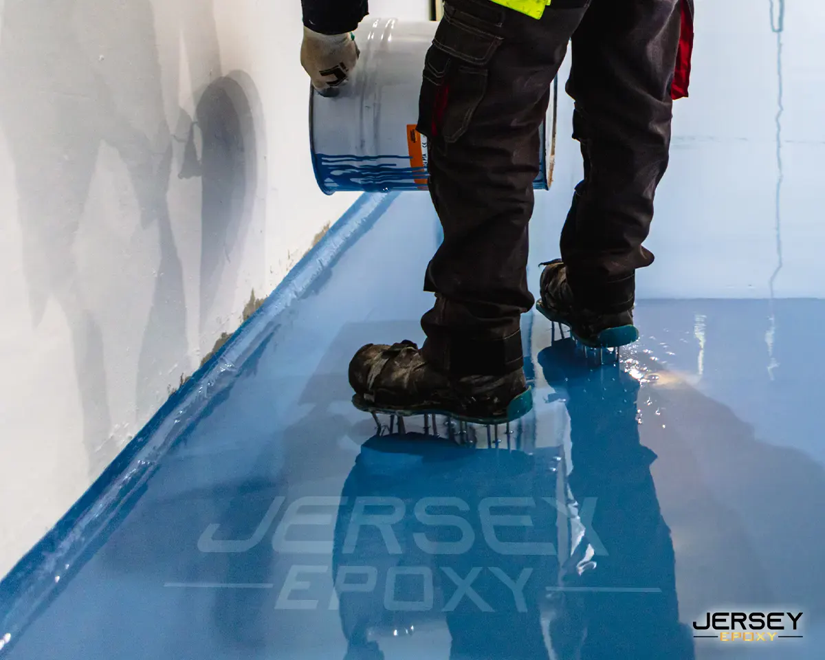 Smooth blue epoxy floor coating being applied in a commercial space by a worker.