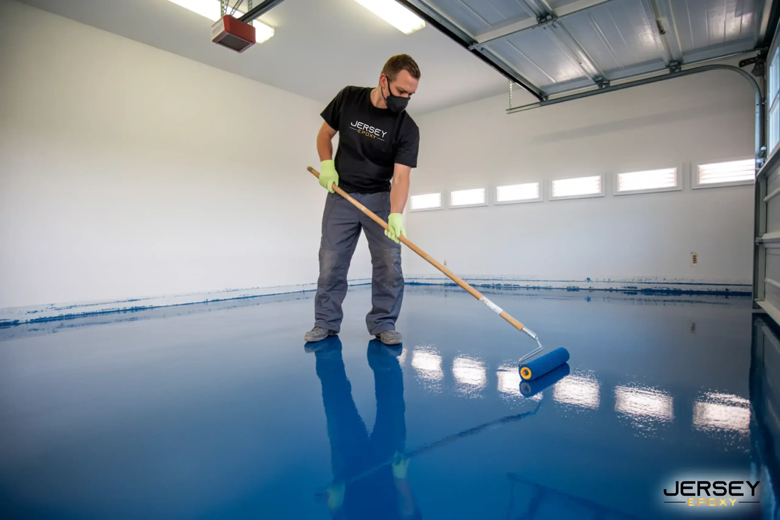 Vibrant blue epoxy floor coating being applied in a spacious garage with a roller.