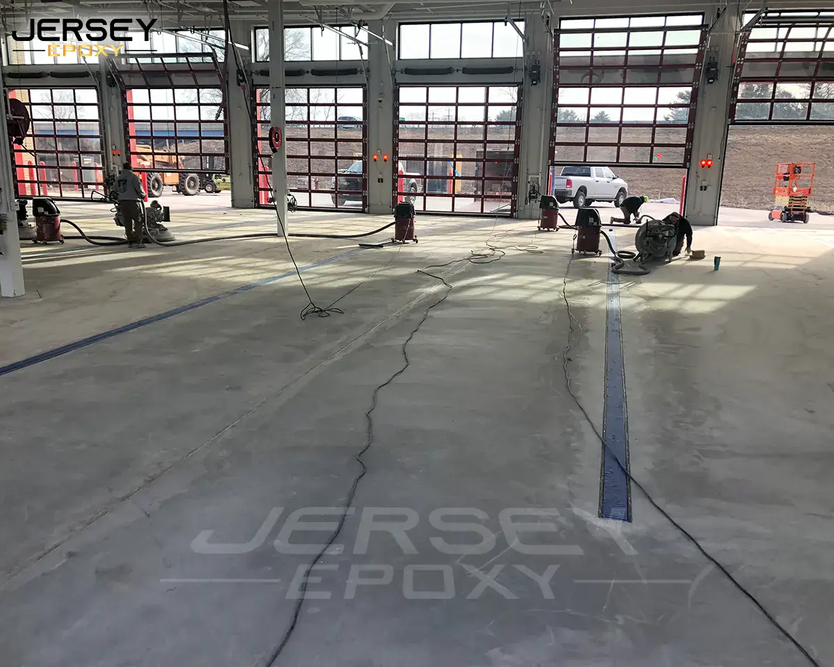 Seamless epoxy flooring being applied in a commercial garage with large open doors and multiple workers.